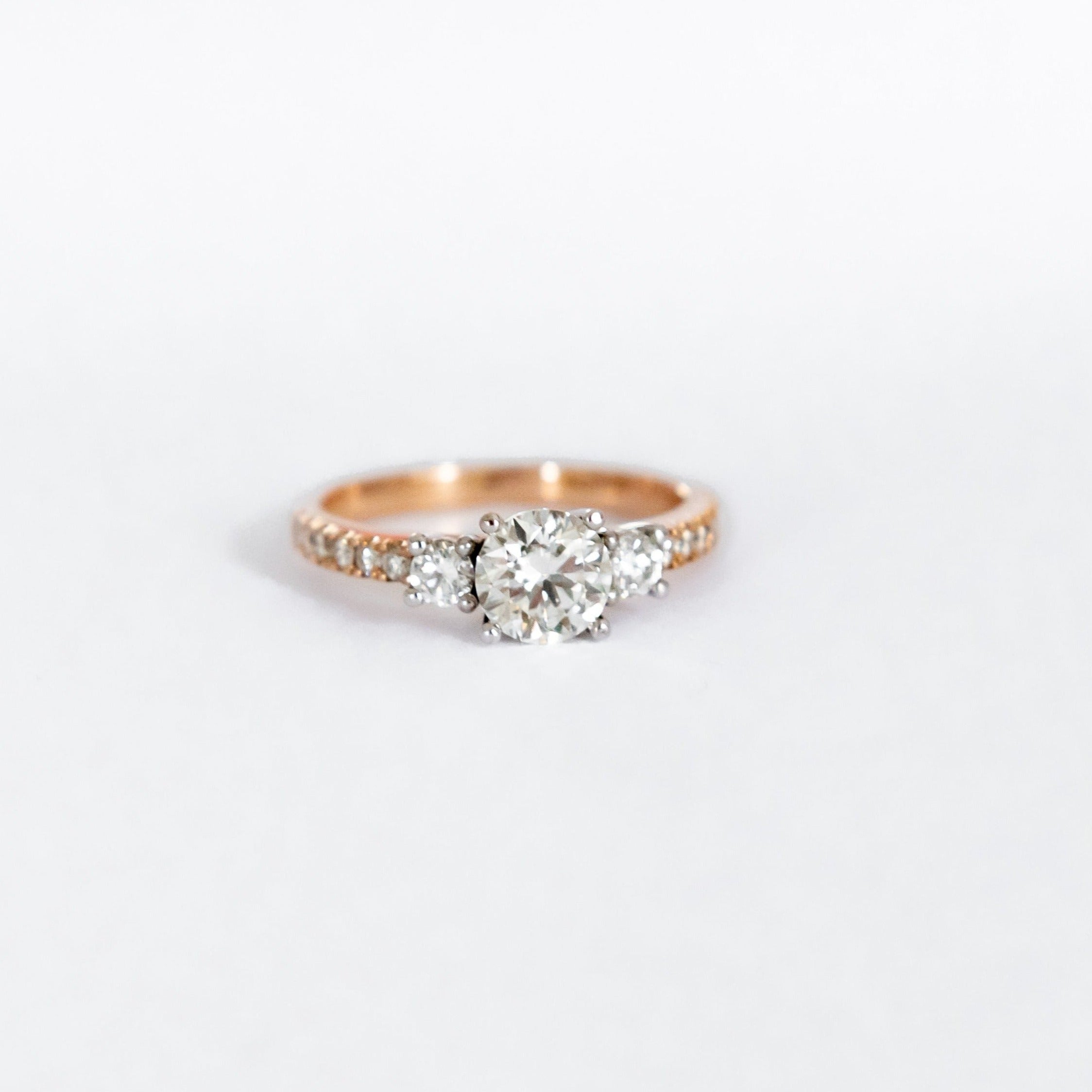 18ct rose gold ring with a 1.02ct round brilliant cut diamond as the centre stone. Two diamonds equalling 0,21ct make up this trilogy in a band of 0,018ct diamonds.