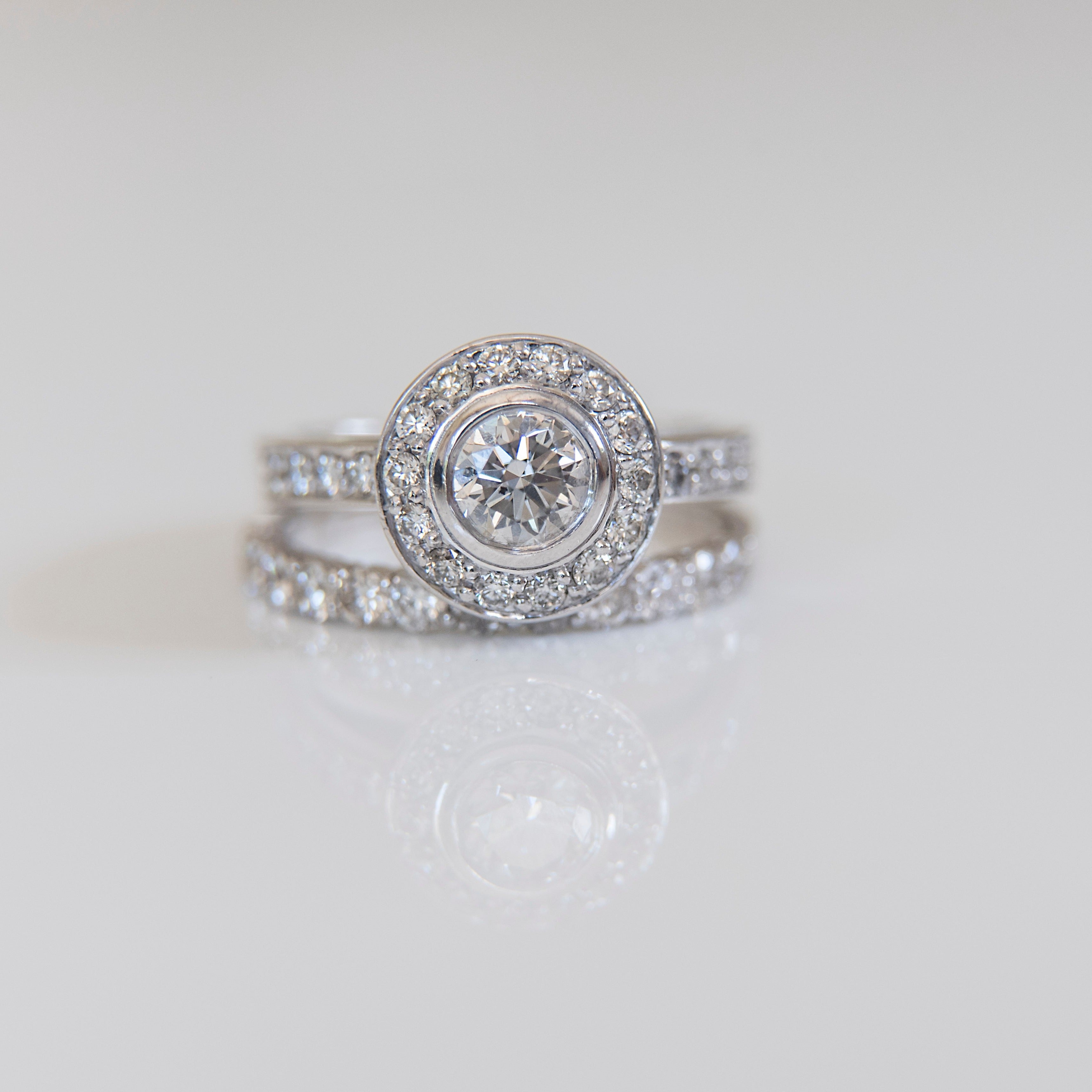  platinum ring with a 1ct cushion cut diamond as the centre stone and a halo of diamonds surrounding the centre stone as well as along the band.