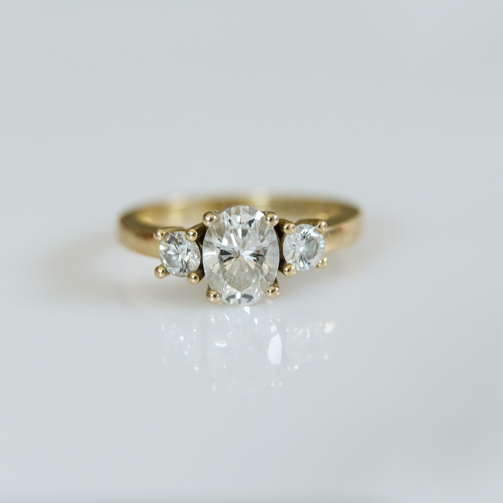 18ct yellow gold trilogy ring with 0.90ct oval cut diamond as the centre stone flanked by two smaller diamonds.