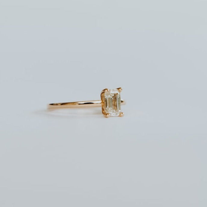 Side view of 18ct yellow gold solitaire ring with 0,72ct claw set emerald cut diamond with a fine rounded band