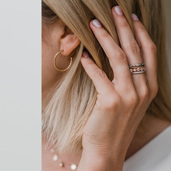  9ct yellow gold Twist Huggie Earrings on ladies ear with rings on fingers